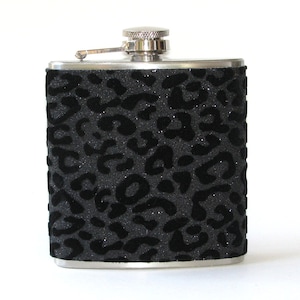 May include: A black and silver flask with a leopard print design. The flask is made of metal and has a screw-on cap.