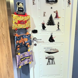 May include: A white door with a room number "6598" and various Disney princess and Star Wars character stickers. There are also three colorful bags hanging on the door with the names "Terry" and "Heather" written on them.