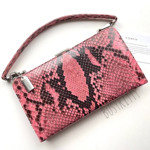 May include: A pink snakeskin clutch purse with a silver top clasp and a short silver chain strap. The purse has the Coach logo on the front.