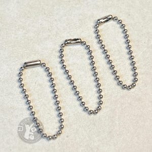 May include: Three silver ball chain keychains of different lengths. The chains are made of small, round metal beads.