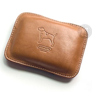 May include: A brown leather Coach wallet with a dog silhouette and the text "COACH EST. 1941" embossed on the front.