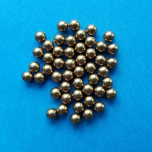May include: A collection of small, shiny, golden-colored metal balls scattered on a bright blue surface. The spheres are evenly sized and reflect light, creating highlights. The overall effect is a display of small, metallic spheres.