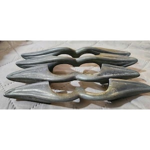 May include: A set of four identical gray metal drawer pulls arranged in a stack. Each pull features a curved, elongated shape with a central cutout and a textured, weathered finish, showcasing a consistent design across all four hardware pieces.
