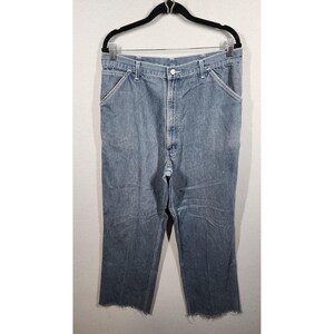 May include: Light blue denim jeans with a straight leg and a raw, unfinished hem. The jeans are hanging on a black hanger against a plain white background. The jeans have classic five-pocket styling.