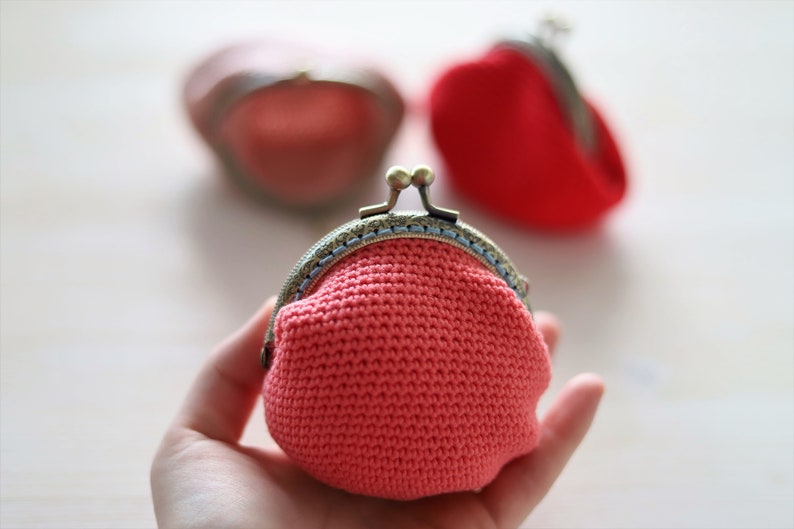 May include: A pink crocheted coin purse with a silver clasp and blue trim.