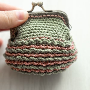 May include: A small crocheted coin purse with a metal clasp. The purse is green with a pink trim and a sparkly finish.