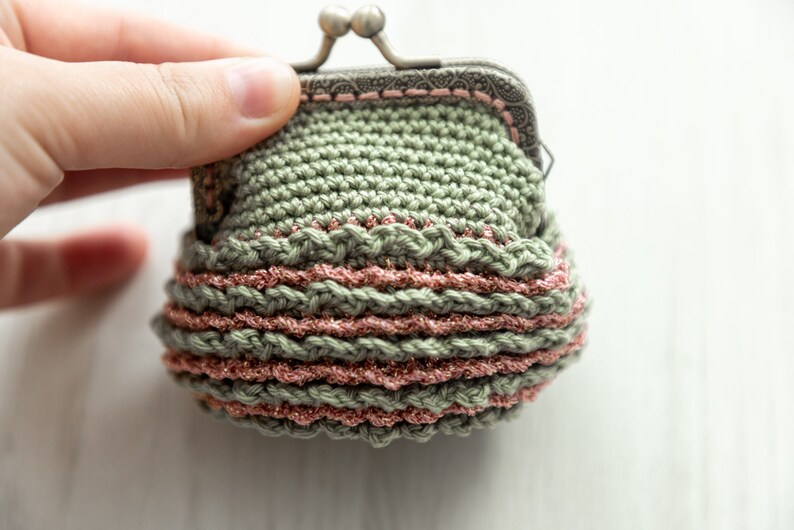 May include: A small crocheted coin purse with a metal clasp. The purse is green with a pink trim and a sparkly finish.