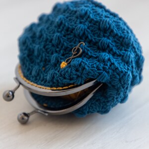 May include: A blue crocheted coin purse with a metal clasp and a gold musical note charm.