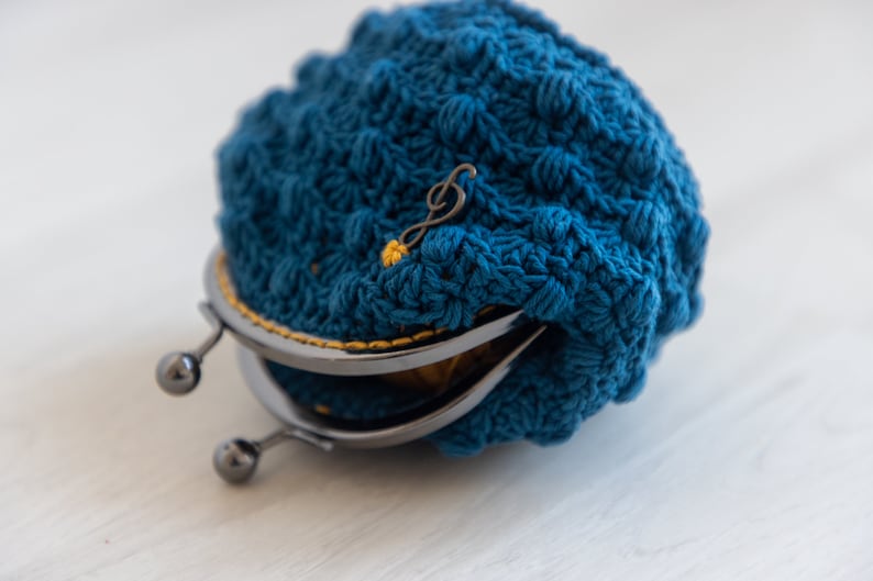 May include: A blue crocheted coin purse with a metal clasp and a gold musical note charm.