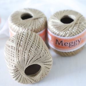 May include: Three spools of gold thread with a label that reads "Meggu" on one of the spools.