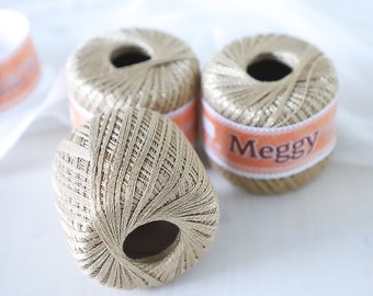 May include: Three spools of gold thread with a label that reads "Meggu" on one of the spools.
