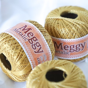 May include: Three spools of gold metallic thread labeled "Meggy Metallic" with a pink and orange design on the label.