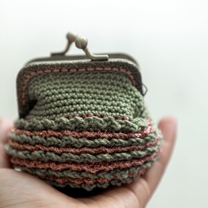 May include: A small green crocheted coin purse with a pink and silver trim. The purse has a metal clasp.