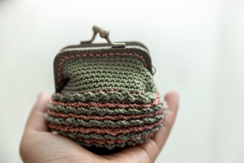May include: A small green crocheted coin purse with a pink and silver trim. The purse has a metal clasp.