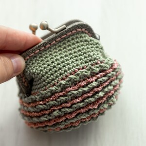 May include: A crocheted coin purse with a green body and pink trim. The purse has a metal clasp.