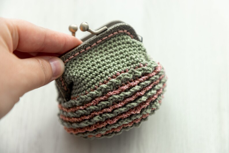 May include: A crocheted coin purse with a green body and pink trim. The purse has a metal clasp.