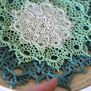 May include: Three crocheted doilies in shades of green and white, layered on top of each other. The doilies are circular and have intricate patterns.