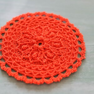 K&ouml;nnte beinhalten: Eine leuchtend orangefarbene geh&auml;kelte Tischdecke mit einem runden Design. Die Tischdecke hat eine zarte Spitzenborte am Rand.