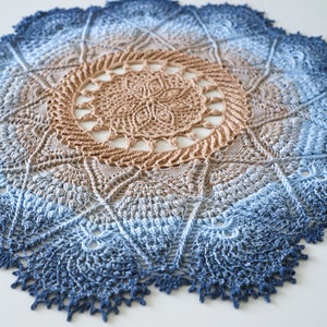 May include: A large, crocheted doily in shades of blue and brown. The doily has a circular shape with a central design and a scalloped edge.
