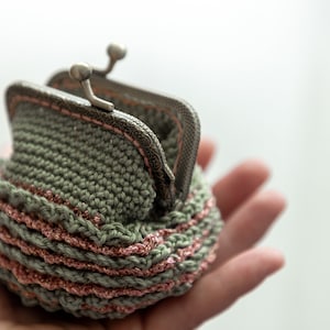 May include: A small crocheted coin purse with a silver clasp. The purse is green with a pink trim.