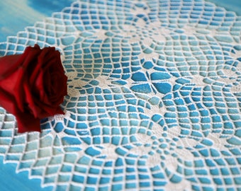 May include: A single red rose lies on a white crocheted doily with a blue background.