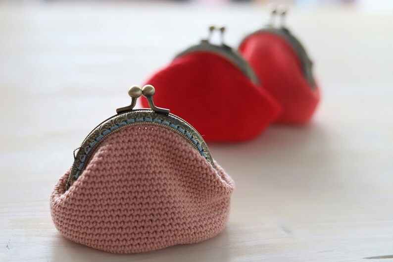 May include: Three crocheted coin purses with metal clasps. The purses are pink, red, and red. The pink purse has a blue trim around the clasp.