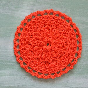 K&ouml;nnte beinhalten: Eine leuchtend orangefarbene H&auml;keldeckchen mit einem runden Design. Die Deckchen hat ein zartes, spitzenartiges Muster und ist perfekt, um jedem Zuhause einen Hauch von handgemachtem Charme zu verleihen.