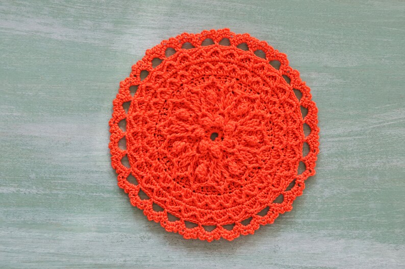 K&ouml;nnte beinhalten: Eine leuchtend orangefarbene H&auml;keldeckchen mit einem runden Design. Die Deckchen hat ein zartes, spitzenartiges Muster und ist perfekt, um jedem Zuhause einen Hauch von handgemachtem Charme zu verleihen.