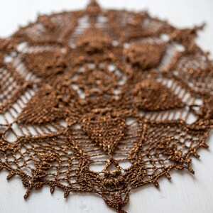 May include: A brown crocheted doily with a delicate, intricate design. The doily is made of a fine, sparkly thread and has a circular shape.