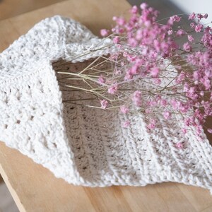 May include: A white crocheted hanging basket with a pink flower bouquet inside. The basket has a loop handle and a textured design.