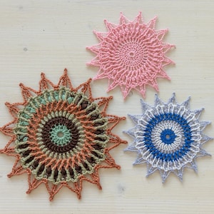May include: Three crocheted doilies in different colors and patterns. The doilies are pink, brown and green, and blue and white.