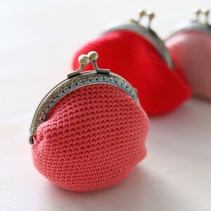 May include: Three crocheted coin purses with metal clasps. The purses are pink, red, and coral.