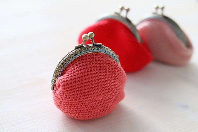 May include: Three crocheted coin purses with metal clasps. The purses are pink, red, and coral.