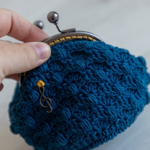 May include: A blue crocheted coin purse with a metal clasp and a small gold musical note charm.