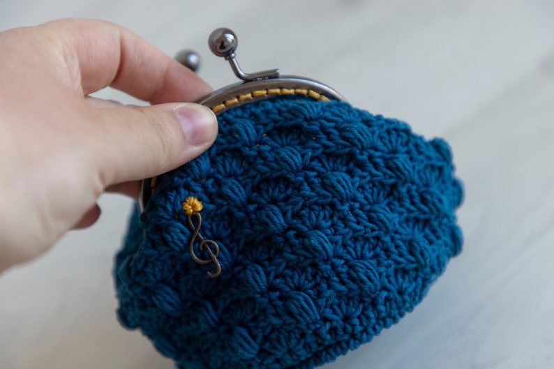 May include: A blue crocheted coin purse with a metal clasp and a small gold musical note charm.