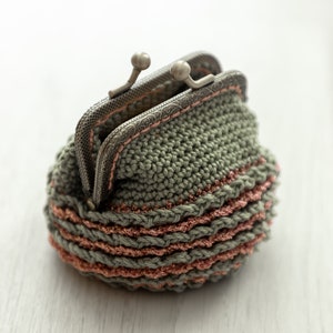 May include: A small crocheted coin purse with a metal clasp. The purse is green with pink stripes.