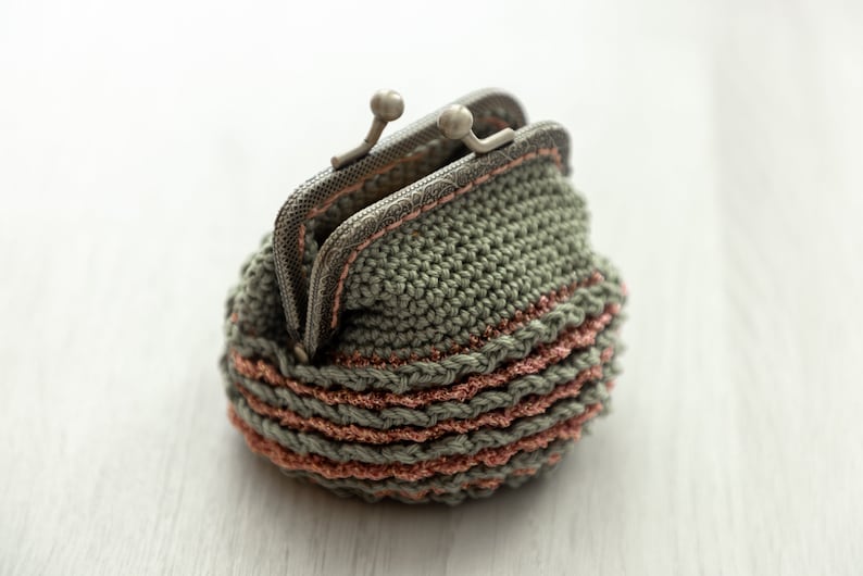 May include: A small crocheted coin purse with a metal clasp. The purse is green with pink stripes.