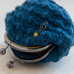 May include: A blue crocheted coin purse with a metal clasp and a musical note charm.