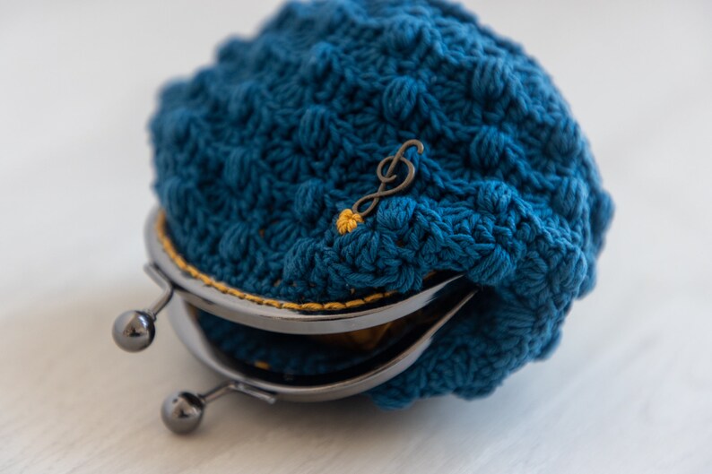 May include: A blue crocheted coin purse with a metal clasp and a musical note charm.