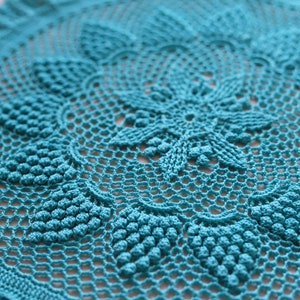 May include: A teal crocheted doily with a delicate floral design. The doily has a circular shape and is made with a fine yarn.