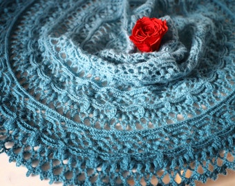 Puede incluir: Un chal de ganchillo azul turquesa con un delicado patrón de encaje y una rosa roja en la parte superior.