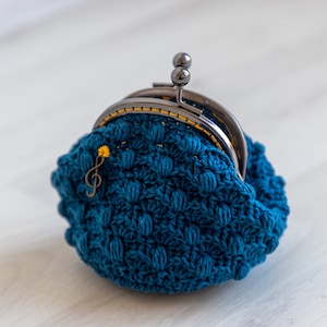 May include: A teal blue crocheted coin purse with a silver clasp and a small gold musical note charm.