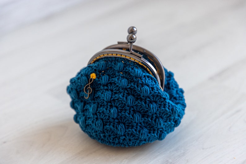 May include: A teal blue crocheted coin purse with a silver clasp and a small gold musical note charm.