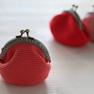 May include: Three crocheted coin purses with metal clasps. The purses are in shades of pink and red.