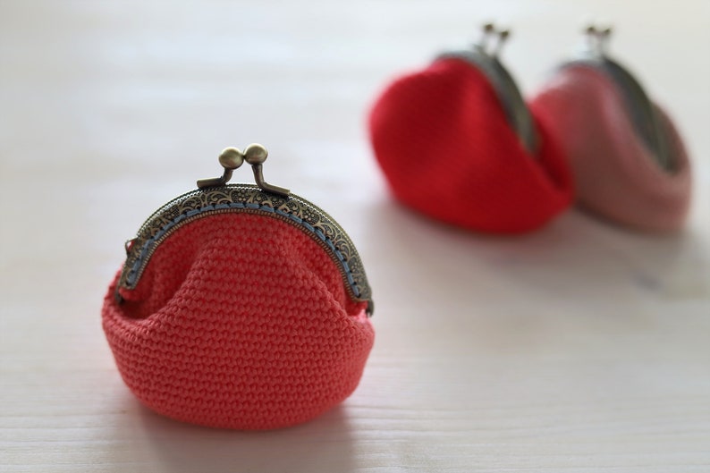 May include: Three crocheted coin purses with metal clasps. The purses are in shades of pink and red.
