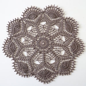 May include: A brown crocheted doily with a delicate, intricate design. The doily is circular and has a scalloped edge.