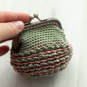 May include: A small crocheted coin purse with a green body and pink trim. The purse has a metal clasp.