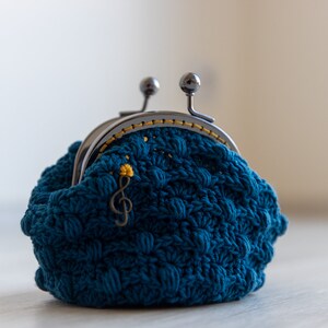 May include: A teal blue crocheted coin purse with a silver clasp and a gold musical note charm.