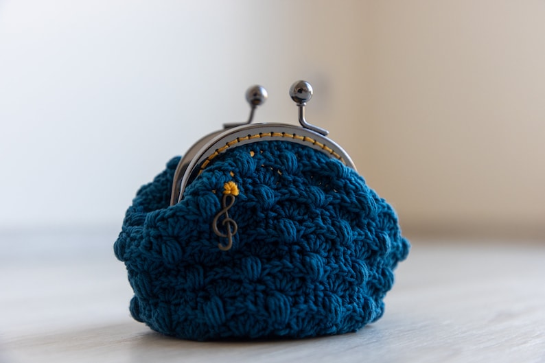 May include: A teal blue crocheted coin purse with a silver clasp and a gold musical note charm.