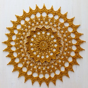 May include: A handmade, golden-yellow crochet doily with a starburst design. The circular doily features a central floral pattern surrounded by multiple layers of openwork and pointed edges. The doily is approximately 12 inches in diameter.